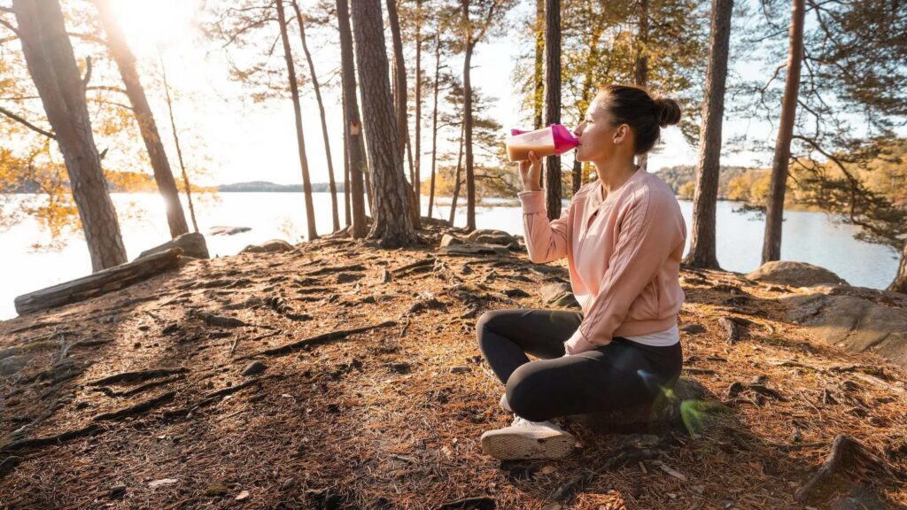 Active woman enjoying a cacao-infused smoothie after outdoor movement, embodying strength and connection to nature.