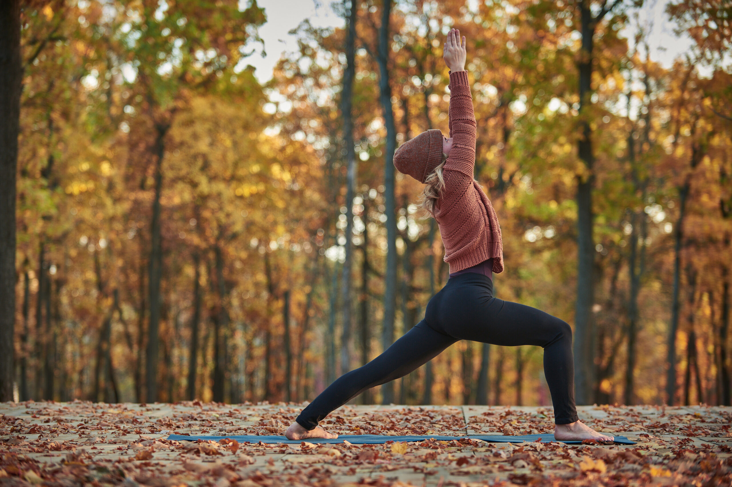 An energetic woman practices yoga amongst the falling leaves of autumn.